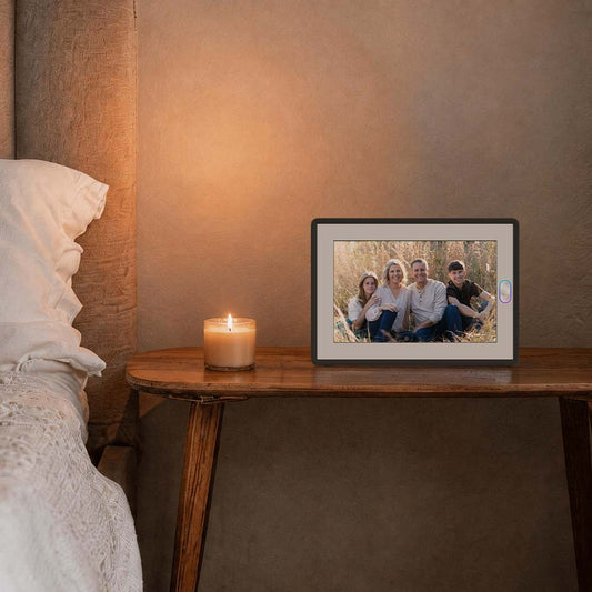 Amivo AI family photo frame on a wooden bedside table displaying a family portrait, next to a lit candle in a cozy home setting.