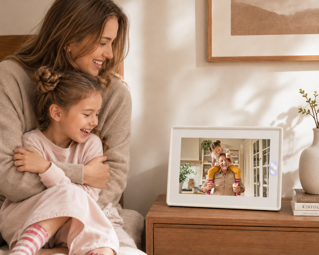 An AmivoFrame smart photo frame displaying a family photo on a minimalist wooden desk with a notebook and desk lamp.