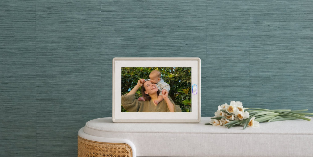 An AmivoFrame smart photo frame displaying a family photo on a minimalist wooden desk with a notebook and desk lamp.